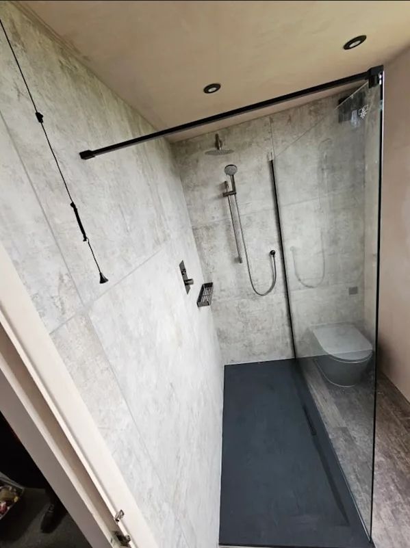 Walk-in glass shower with concrete-effect tiling and black fittings